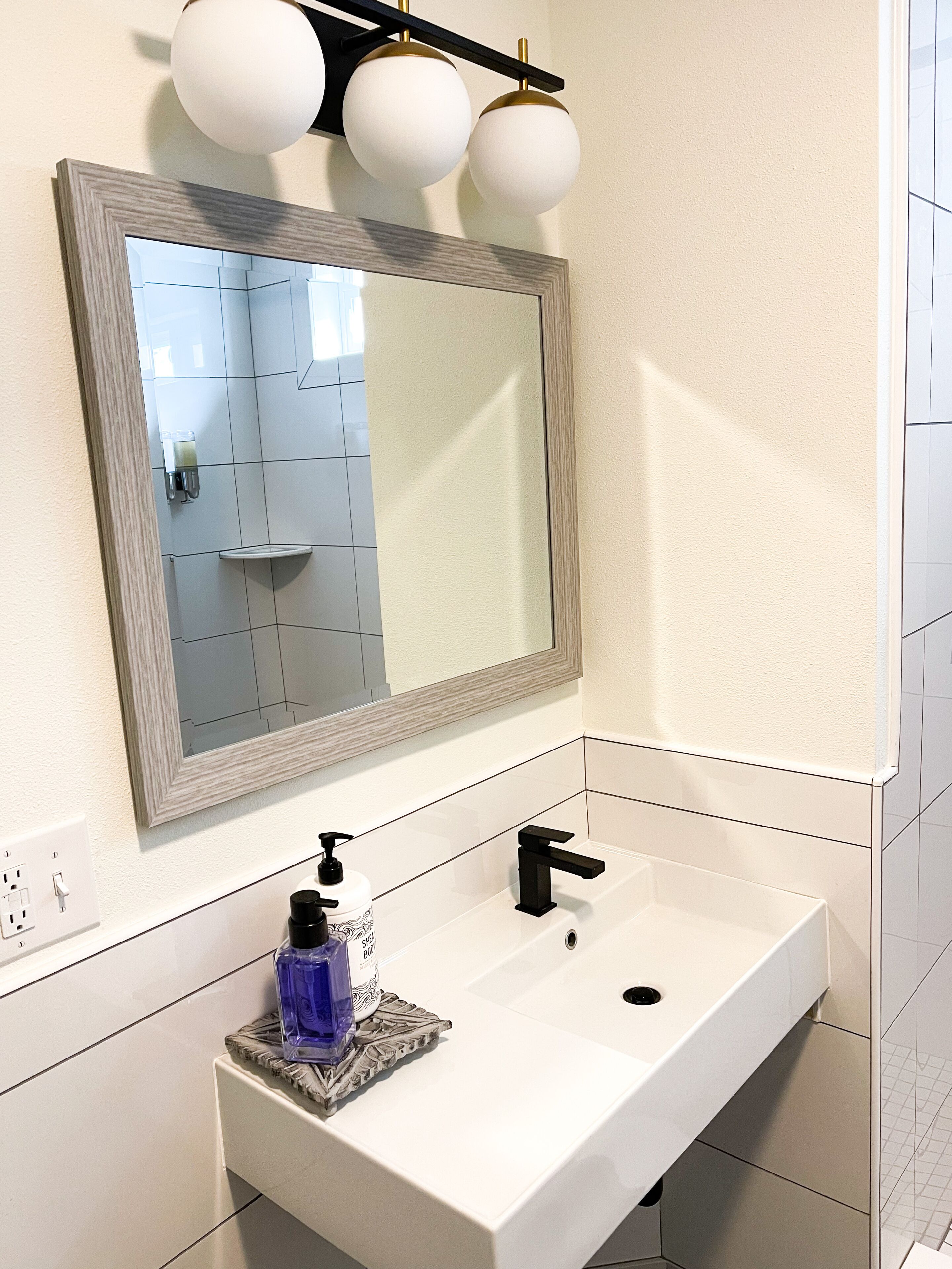 A bathroom with a white sink, a black faucet, a mirror with a wooden frame, and a wall-mounted light fixture.