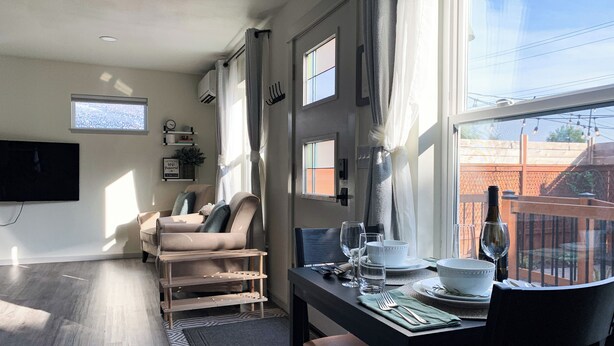 A dining area with a table set for two, a TV mounted on the wall, and a window with curtains. - Washburne Studio: King size comfort and private Hot tub (Springfield)