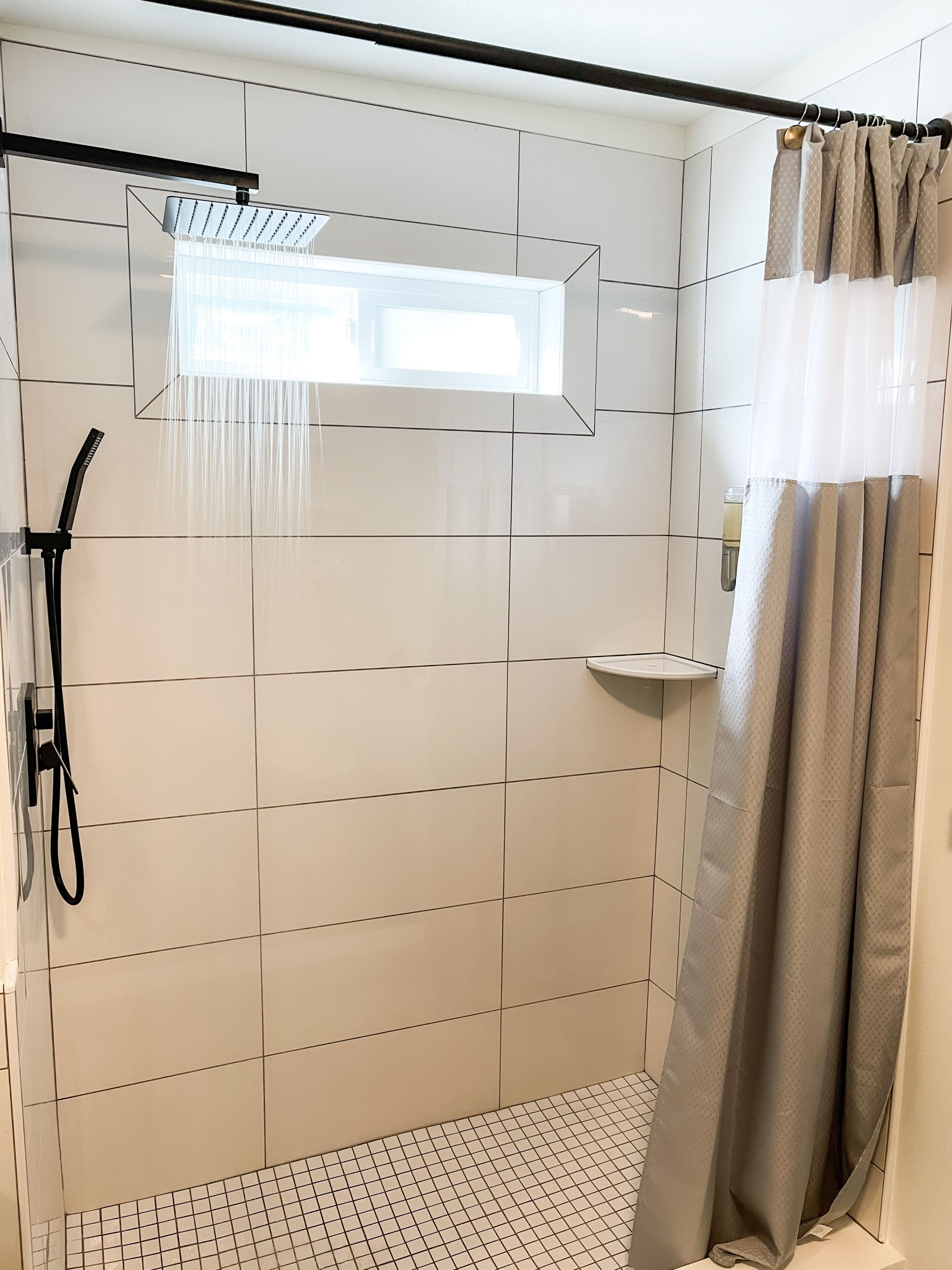 A modern shower area with a glass-enclosed showerhead, a handheld showerhead, and a shower curtain.
