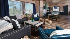 A cozy cabin interior with a sofa, armchair, and wooden coffee table. A kitchen area with a dining table and benches is visible in the background. - Grace Place - Private Indoor Pool, Hot Tub, Views, Theater, and more! (Sevierville)