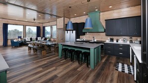 A modern kitchen with wooden flooring, a central island with stools, and a dining area with a bench and chairs. - Grace Place - Private Indoor Pool, Hot Tub, Views, Theater, and more! (Sevierville)