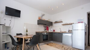 Une cuisine moderne avec une table à manger, des chaises, un téléviseur fixé au mur et un réfrigérateur.