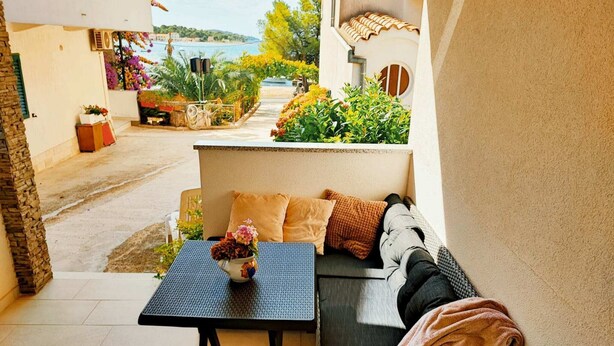 Un balcone con un divano in vimini, un tavolino con un vaso e vista su una zona costiera.
