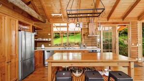 Une cuisine rustique aménagée dans une cabane en bois, avec un grand îlot central, des appareils en acier inoxydable et une vue sur la verdure environnante.