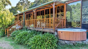 Une terrasse en bois avec un jacuzzi, entourée d’une végétation luxuriante et d’un mur de pierre.