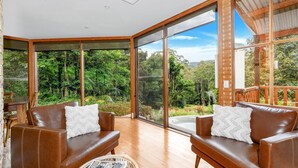 Une pièce spacieuse avec deux canapés en cuir, une table basse en bois et de grandes fenêtres du sol au plafond offrant une vue sur une forêt luxuriante.