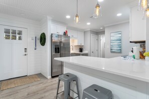 A modern kitchen with white cabinetry, a stainless steel refrigerator, and pendant lighting.