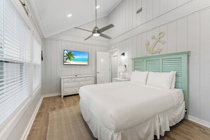 A bedroom with a bed, a ceiling fan, a TV, a dresser, and a door.