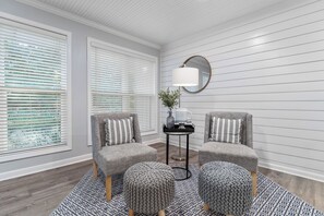 A room with two grey armchairs, a small black side table with a lamp, and a round mirror on the wall.