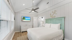 Ein Schlafzimmer mit einem Bett, einem Deckenventilator, einem Fernseher, einer Kommode und einer Tür.