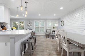 A modern kitchen with white cabinetry, a central island with stools, pendant lighting, and a view to the outside.