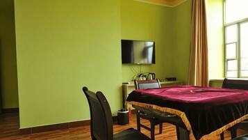 A room with a dining table, chairs, a television mounted on the wall, and a window with curtains.