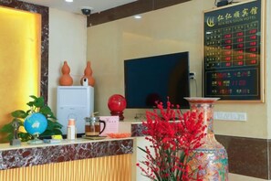 Un mostrador de recepción de hotel con una pantalla digital, un globo terráqueo, un jarrón con flores rojas y un televisor montado en la pared.