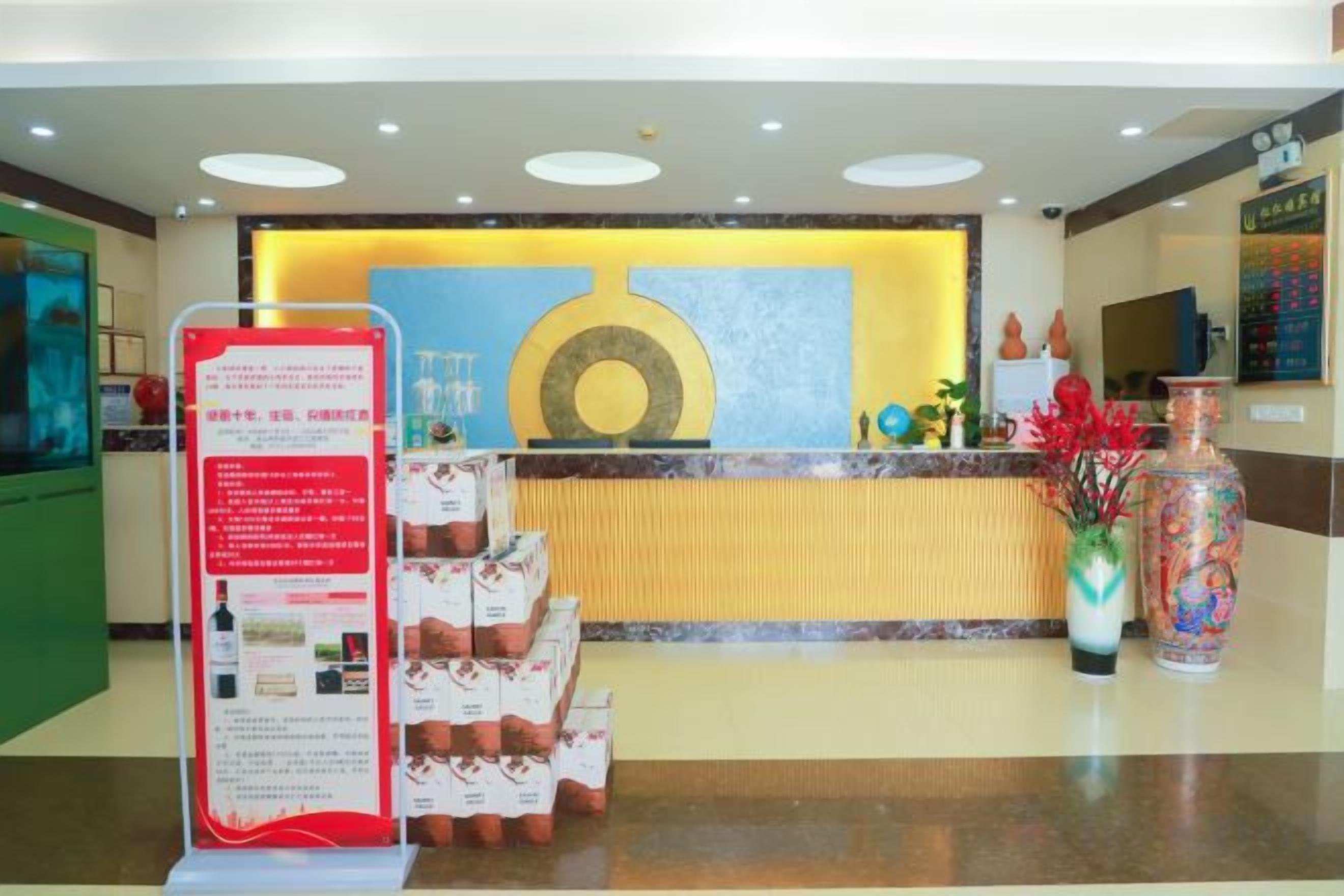 Ein Hotel-Empfangsbereich mit einer Rezeption, Informationsplakaten und einer dekorativen Vase.