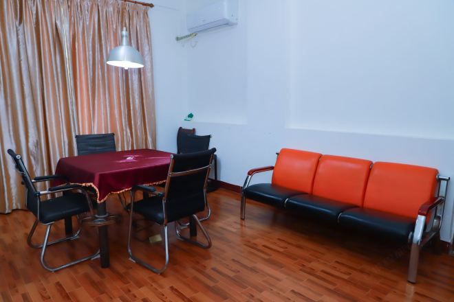 A room with a wooden floor, a table with a red tablecloth, four black chairs, a red sofa, and a hanging lamp.