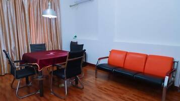 A room with a wooden floor, a table with a red tablecloth, four black chairs, a red sofa, and a hanging lamp.