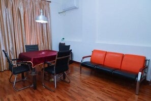 A room with a wooden floor, a table with a red tablecloth, four black chairs, a red sofa, and a hanging lamp. - Renrenshun Hotel (Haifeng)
