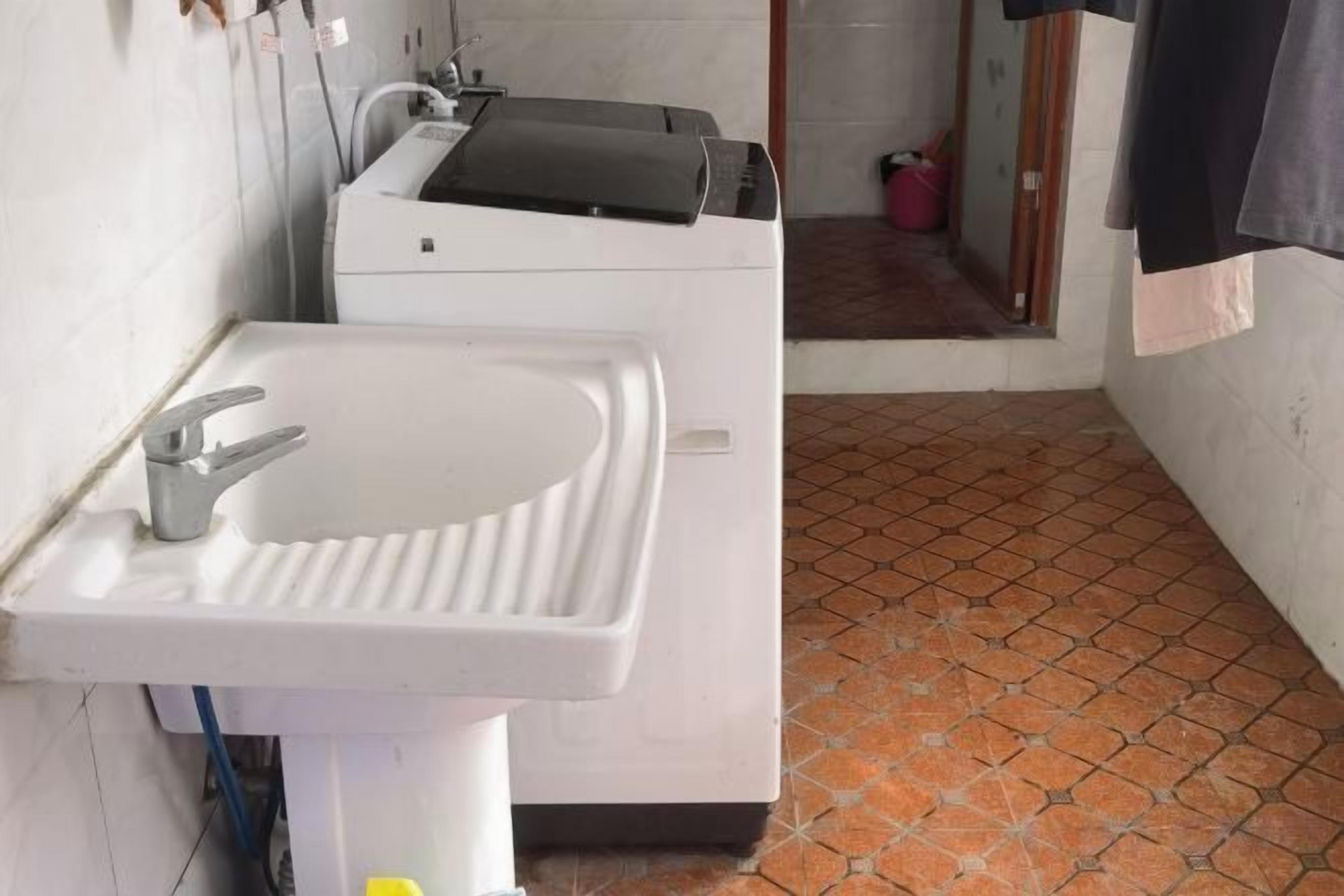 A bathroom with a white sink, a washing machine, and a tiled floor.