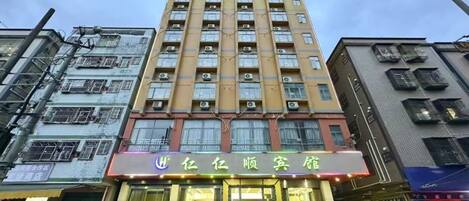 Un hotel de varios pisos con una entrada destacada, unidades de aire acondicionado y una tienda con señalización visible.