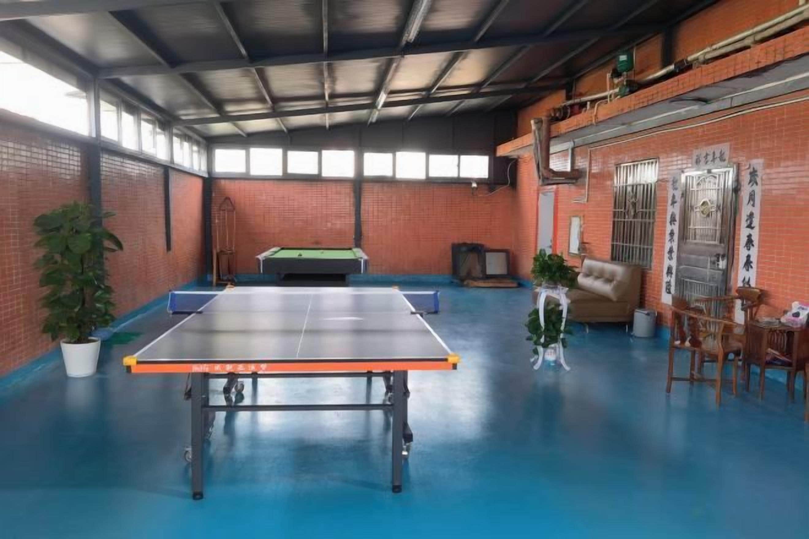 A ping pong table in a room with a blue floor, brick walls, and a door with Chinese characters.