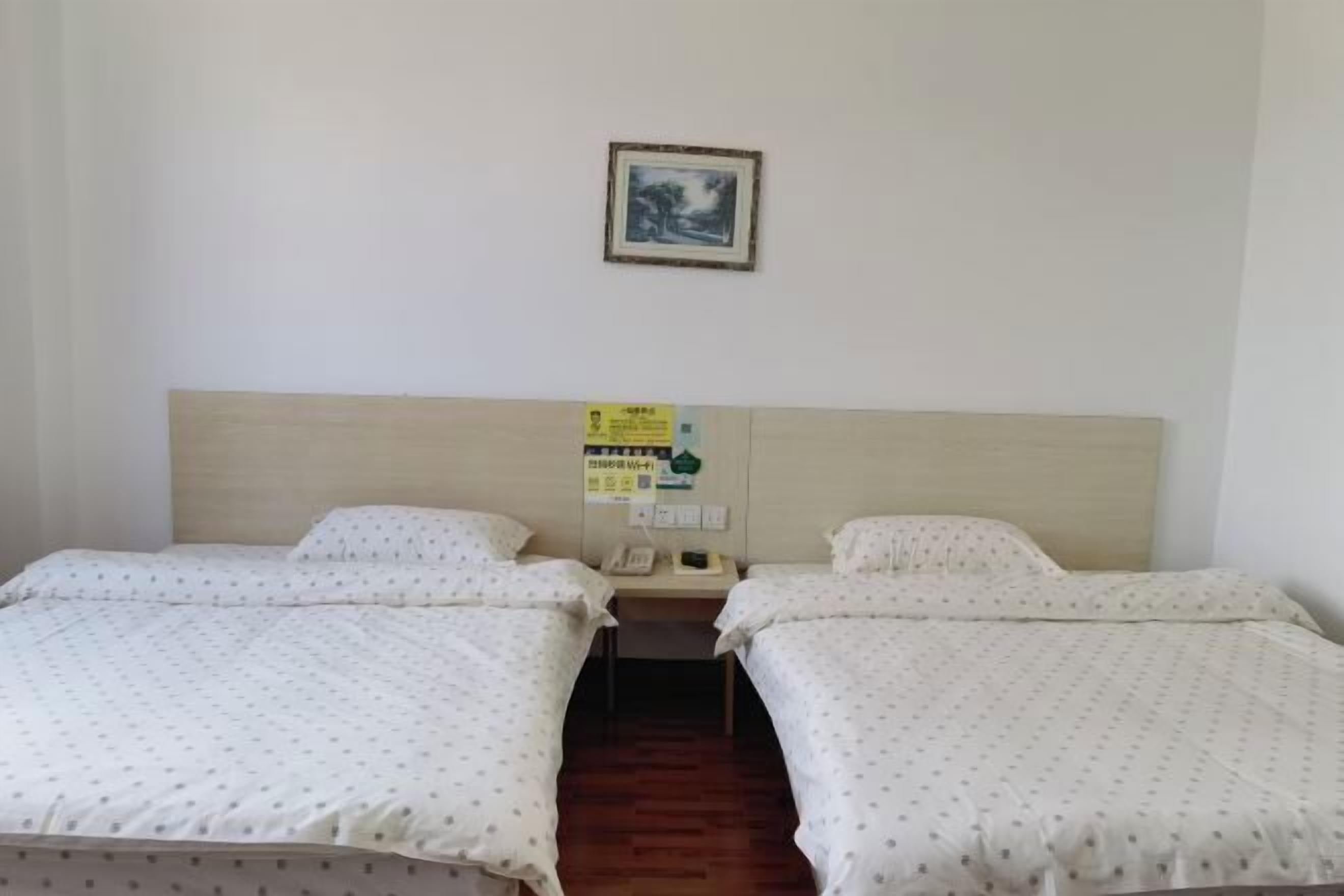 A hotel room with two beds, a wooden headboard, a small desk, and a wall-mounted phone.