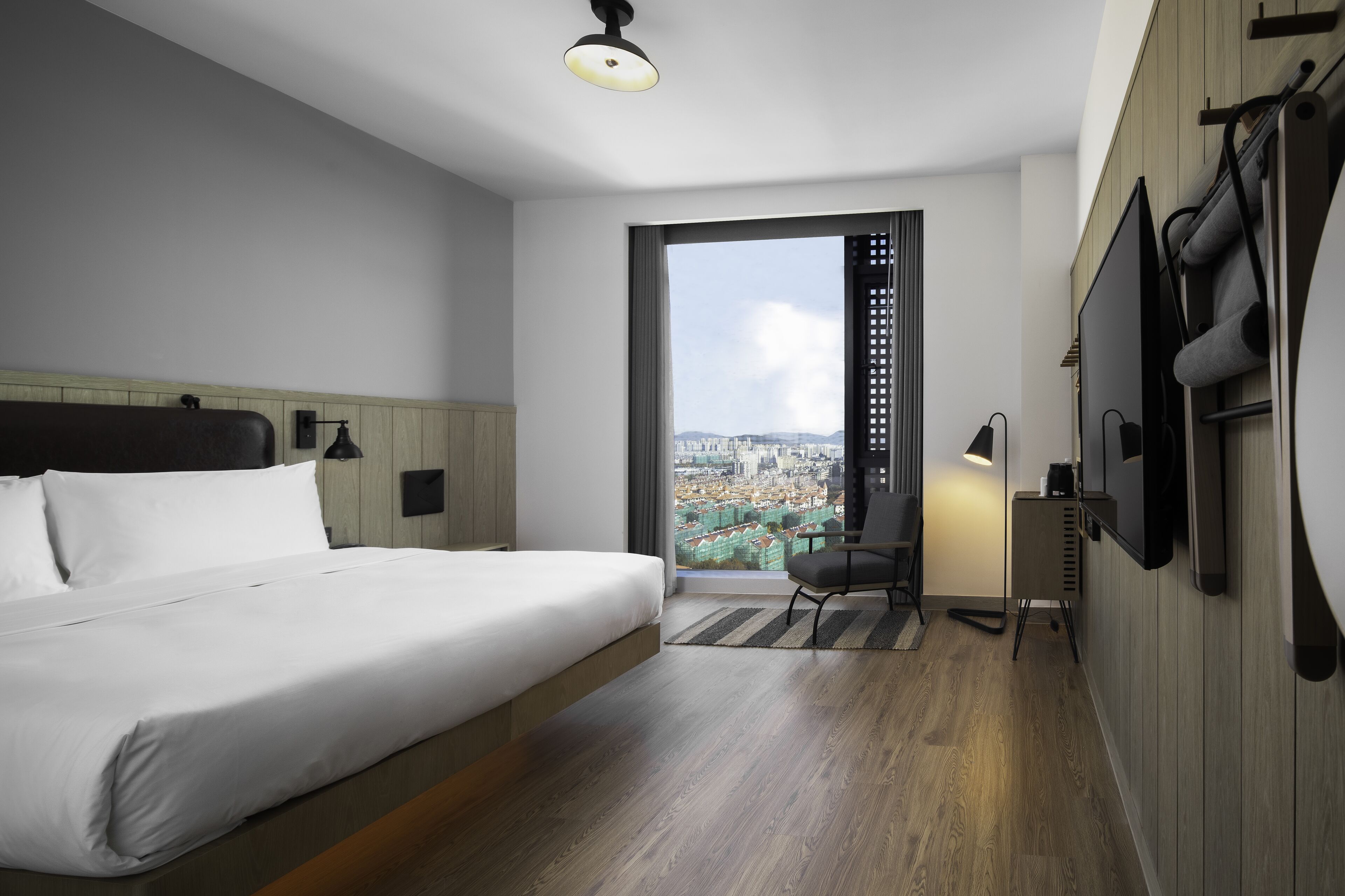 A modern hotel room with a bed, a desk, a chair, and a TV.