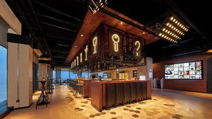 A modern bar area with a wooden bar counter, pendant lighting, and a large digital display wall. - Moxy Nanjing Jiangning (Nanjing)