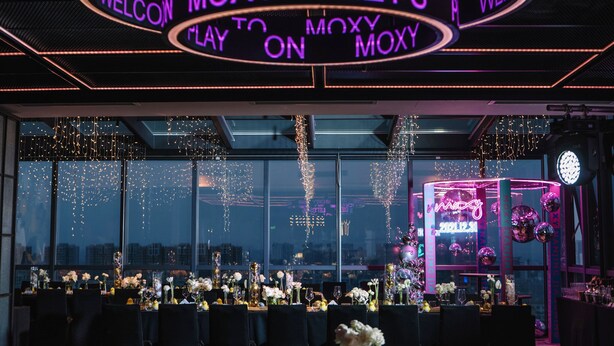 A reception area with a neon sign reading "WELCOME TO MOXY PLAY ON MOXY" and a view of the city through large windows. - Moxy Nanjing Jiangning (Nanjing)