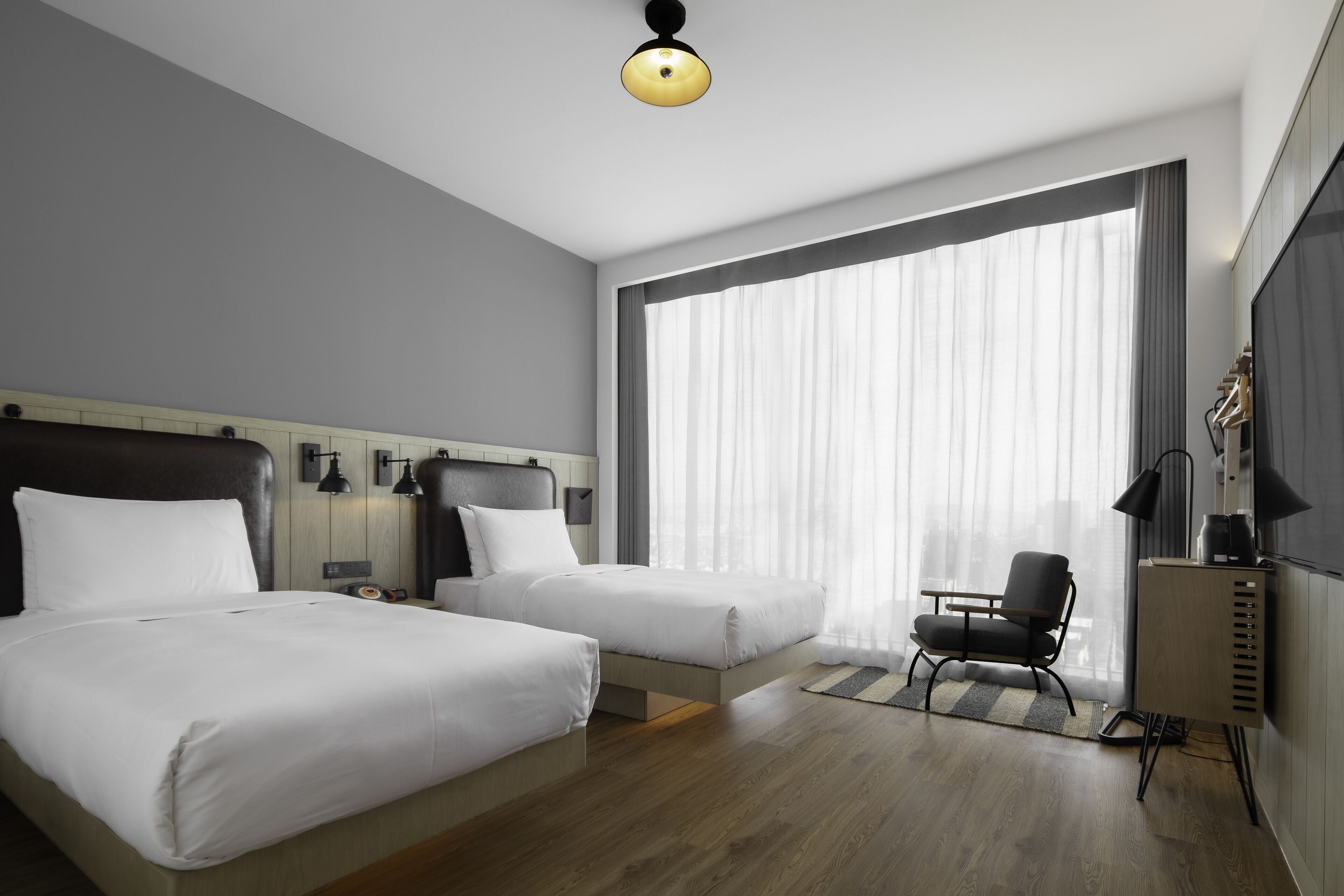 A modern hotel room with two beds, a desk, a chair, and a large window with curtains.