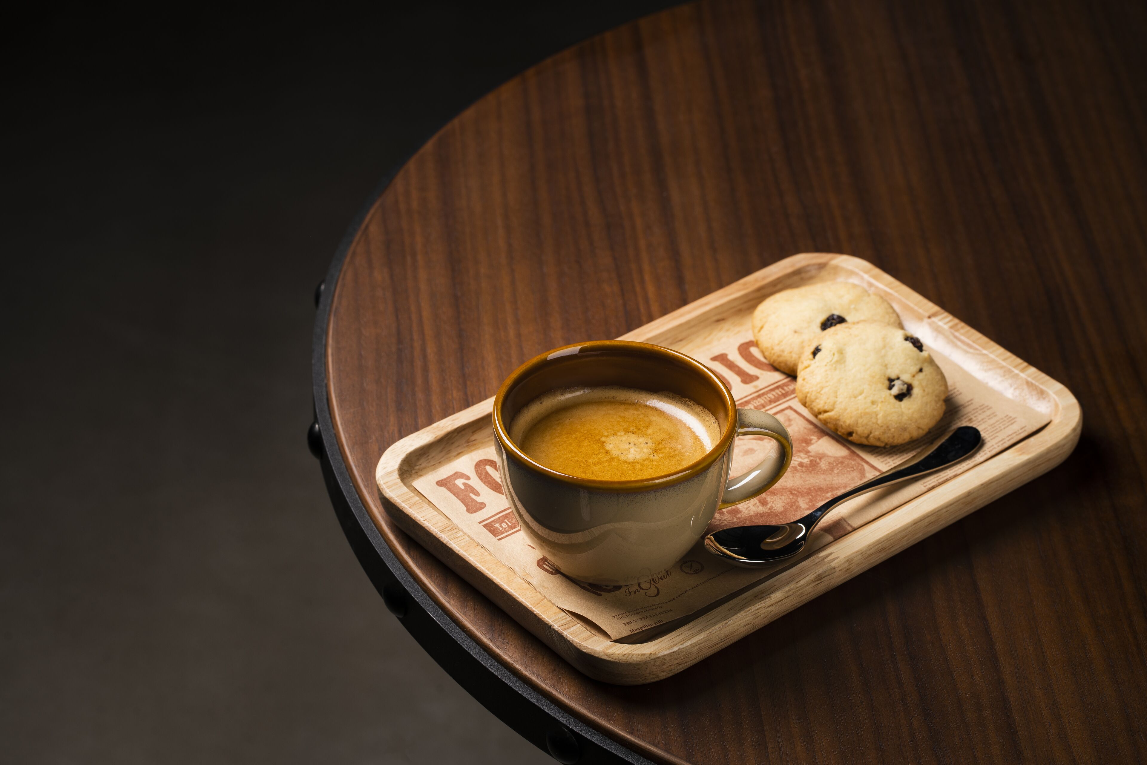 A cup of coffee on a wooden tray with two cookies.