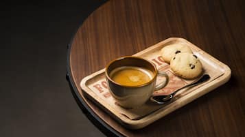 A cup of coffee on a wooden tray with two cookies.