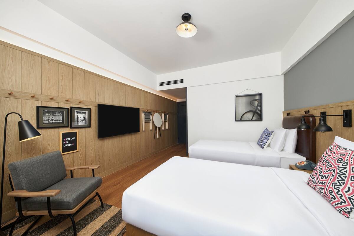 Quarto de hotel moderno com uma cama grande, um sofá, uma escrivaninha e uma televisão de tela plana.