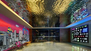 A modern interior with a colorful mural, a bicycle, and a neon sign with various icons. - Moxy Nanjing Jiangning (Nanjing)