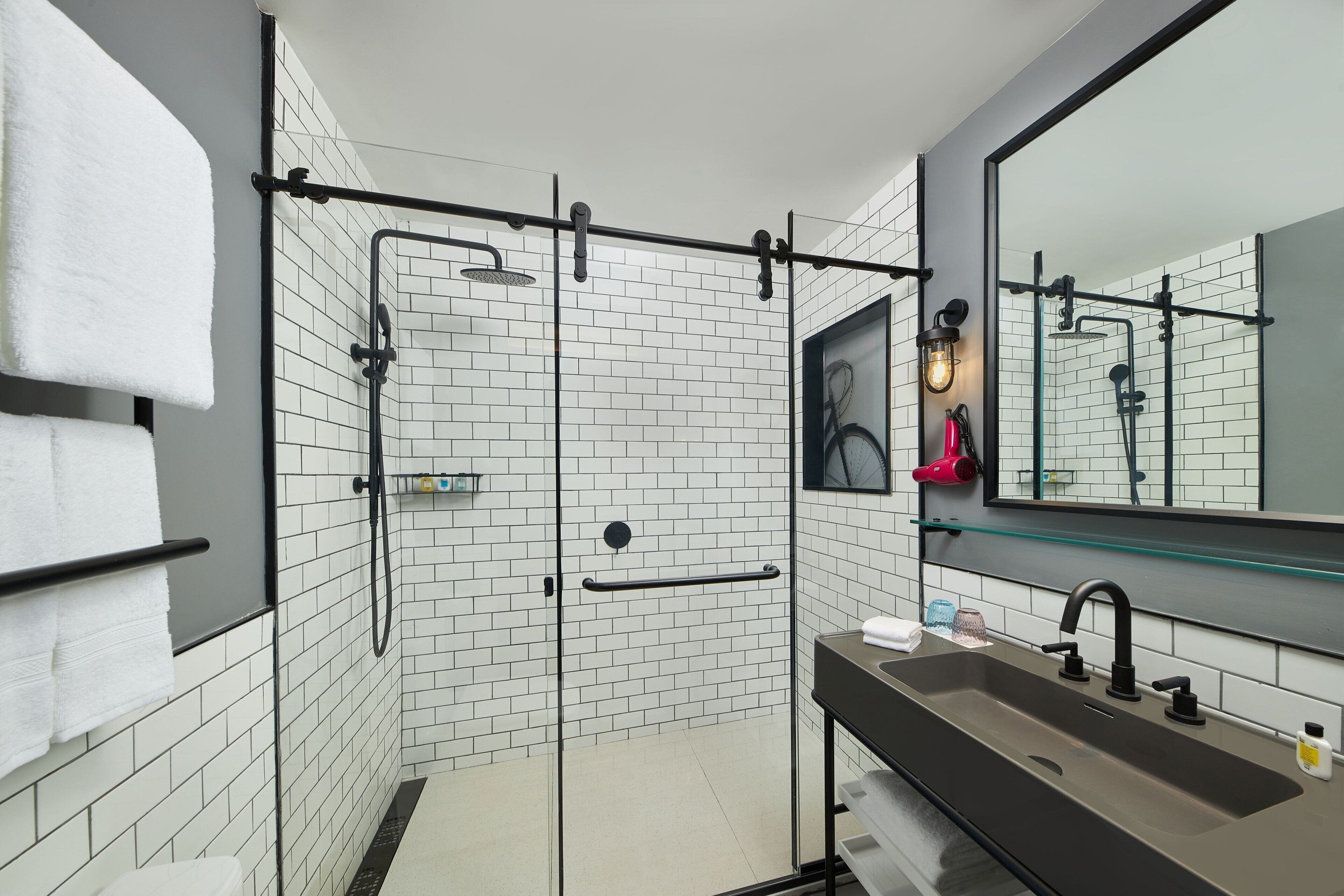 Ein modernes Badezimmer mit einer Glaskabine zur Dusche, einem großen Spiegel und einem Waschbecken mit schwarzem Wasserhahn.