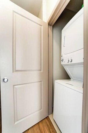 Un lavadero con puerta blanca y lavadora y secadora apiladas.