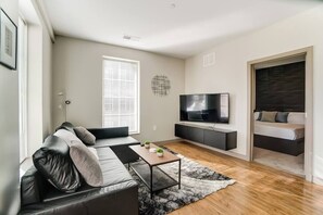 Una sala de estar moderna con un sofá, una mesa de centro, un televisor y una cama al fondo.
