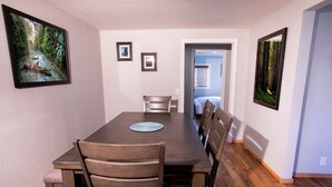 Un comedor con una mesa y sillas de madera, cuadros en las paredes y vistas a otra habitación.