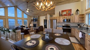 A spacious living area with a fireplace, wooden ceiling, and large windows.