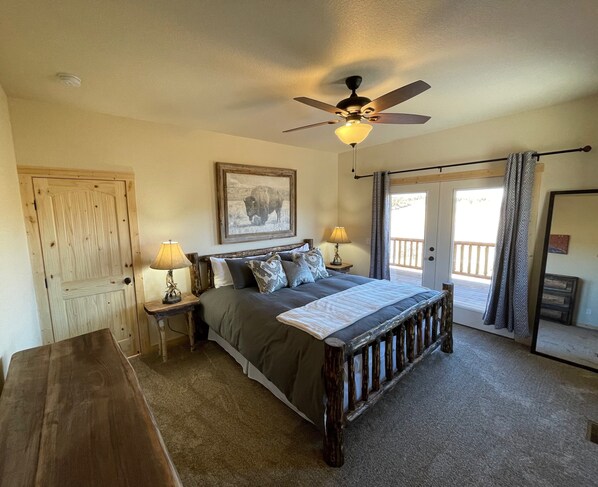 A bedroom with a large bed, a ceiling fan, a wooden bench, a door, and a balcony with curtains.