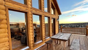 A log cabin with large windows, a deck with a wooden table and benches, and a view of a snowy landscape.