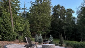 Een rond zitgedeelte buiten met een vuurkuil, twee Adirondack-stoelen en een stenen tafel.