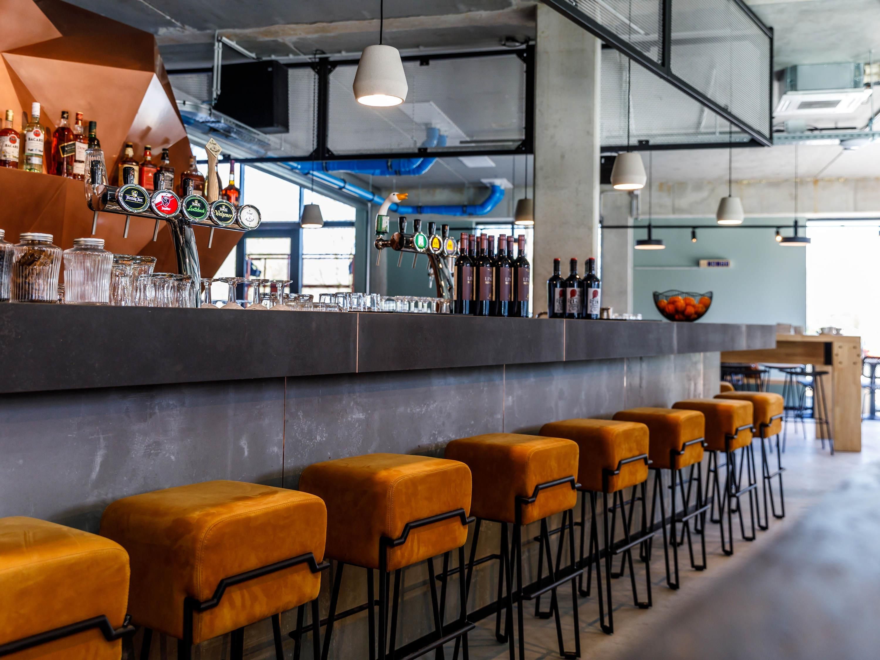 Eine Bar mit Hockern, Flaschen, Gläsern und einer Theke.