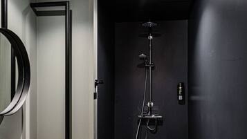 Un baño moderno con tocador de madera, un espejo grande, una cabina de ducha negra y suelo de baldosas.