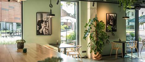 A modern cafe interior with a wooden table, chairs, hanging plants, and artwork on the walls.