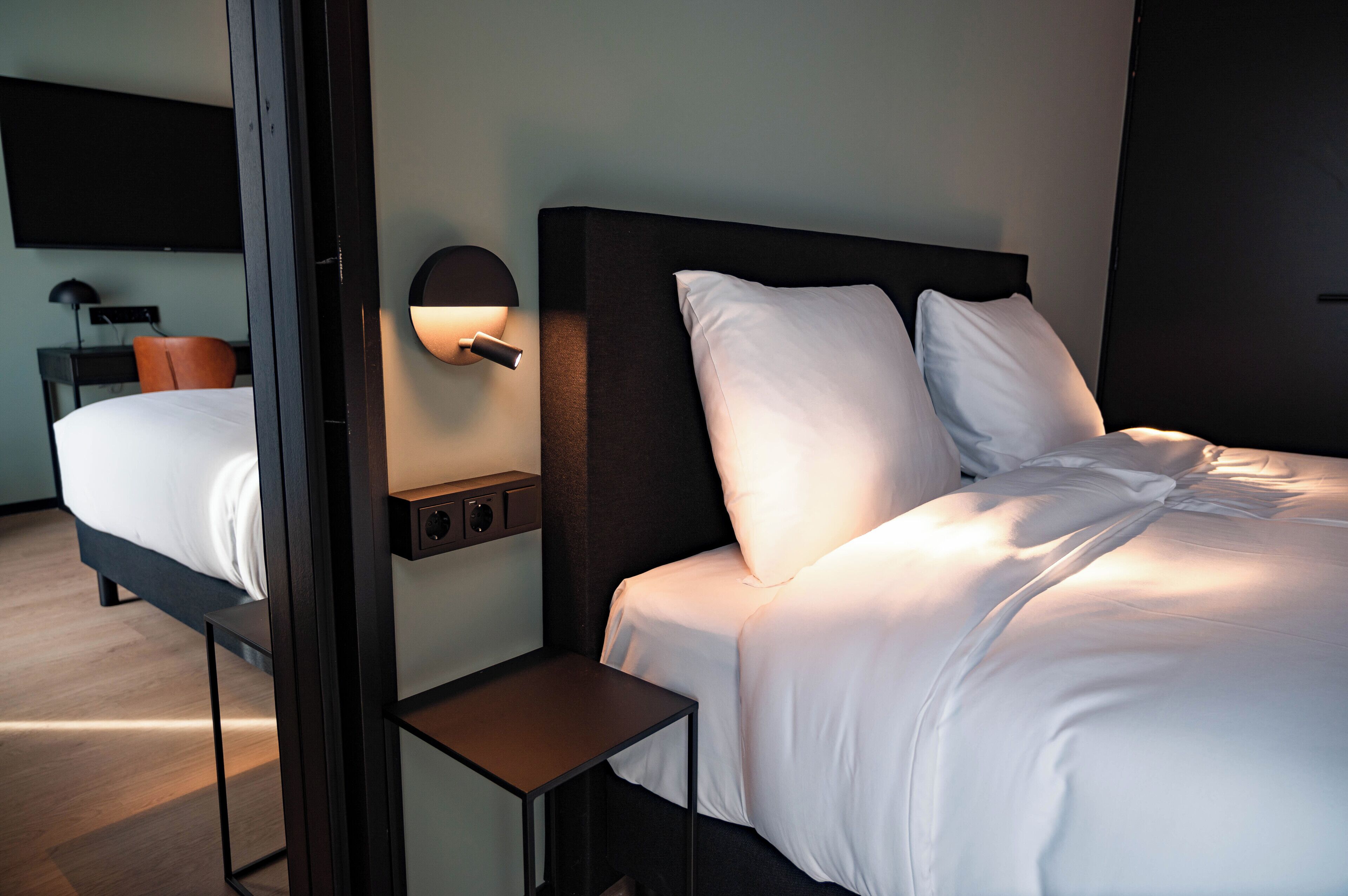 Ein Hotelzimmer mit einem Bett, einem Nachttisch, einer Wandleuchte und einem flachbildschirmfernseher an der Wand.