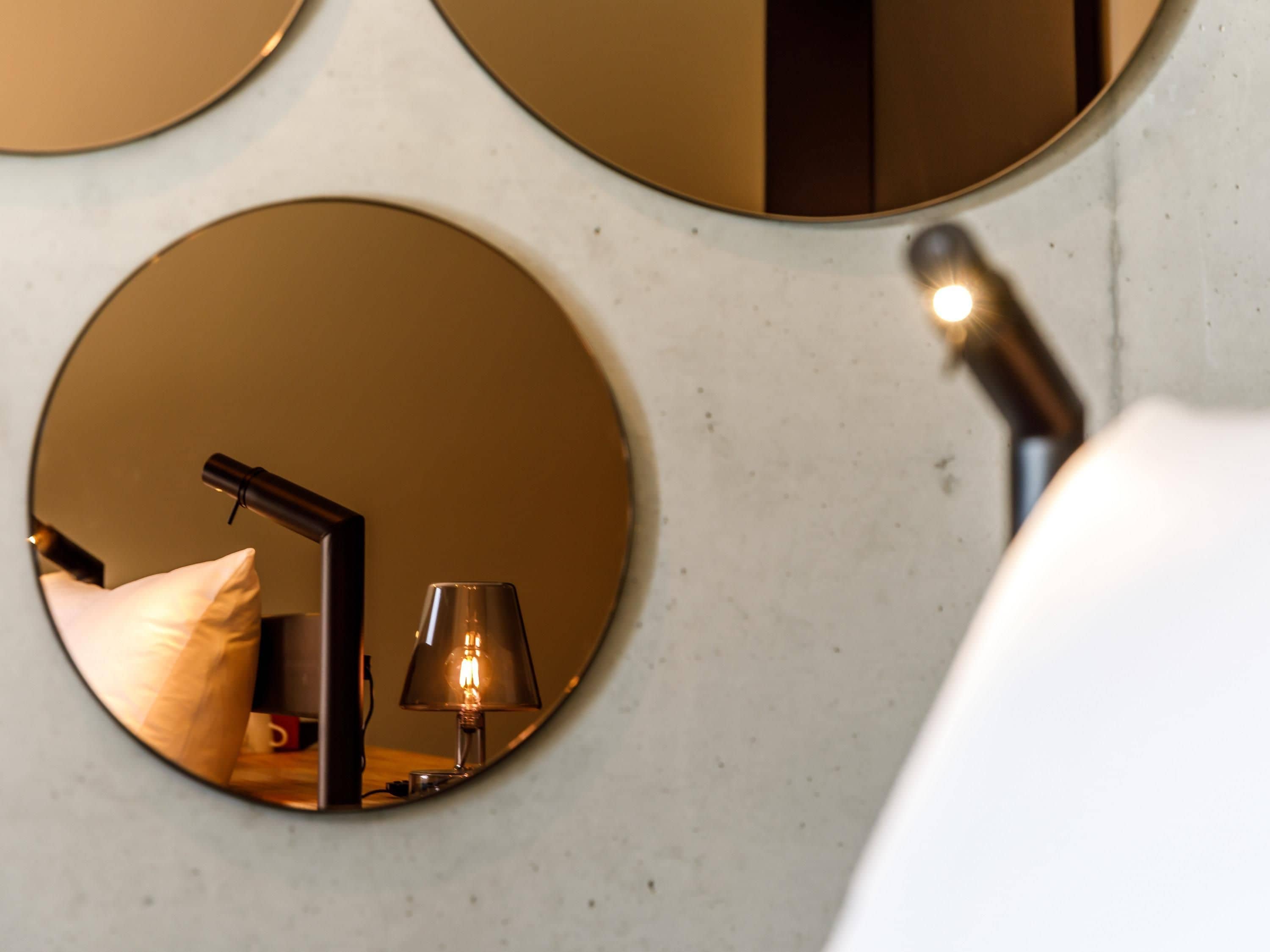 Une salle de bain avec un miroir rond, une lampe et un coussin.