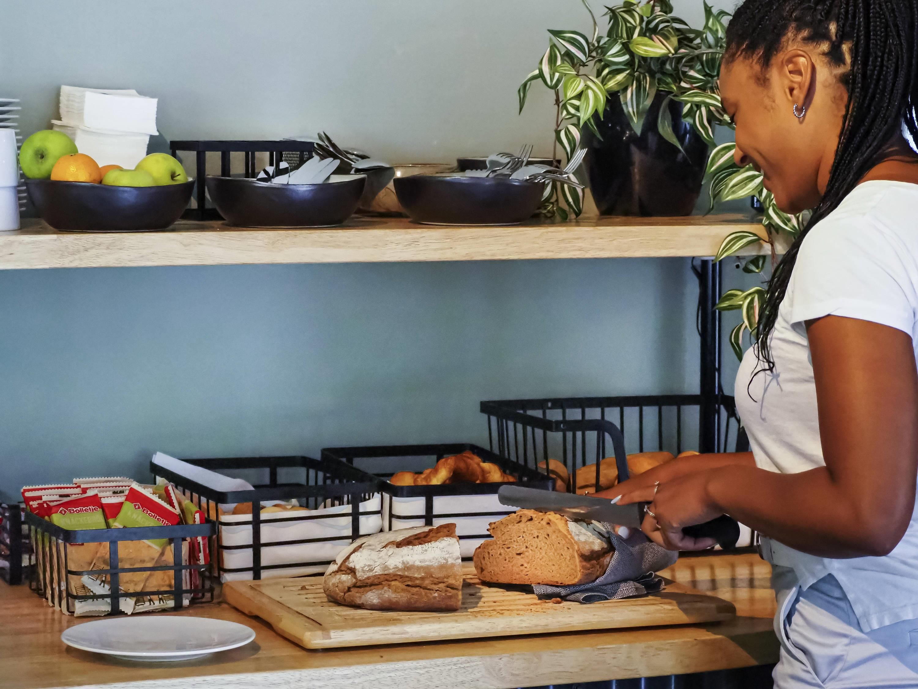 Una cocina con tabla de cortar, pan y una persona cortando pan.