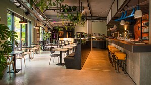 Un café moderno con plantas de interior, una zona de bar y mesas para clientes.