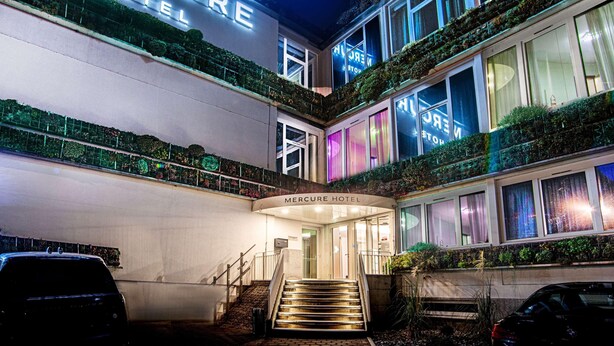 Un hotel con un letrero llamativo, una escalera que lleva a la entrada y un balcón con plantas.