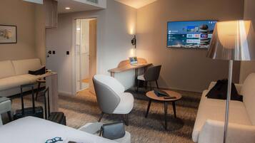 A hotel room with a bed, a desk, a chair, a sofa, a TV, and a lamp.